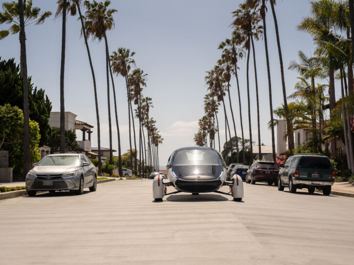 Ein futuristisches Fahrzeug fährt in der Sonne auf palmengesäumter Straße