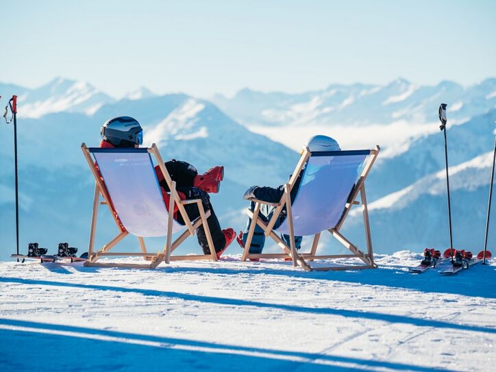 Zwei Menschen von hinten in einem Liegestuhl, sie blicken auf die verschneiten Berge des Skigebiets Wilder Kaiser