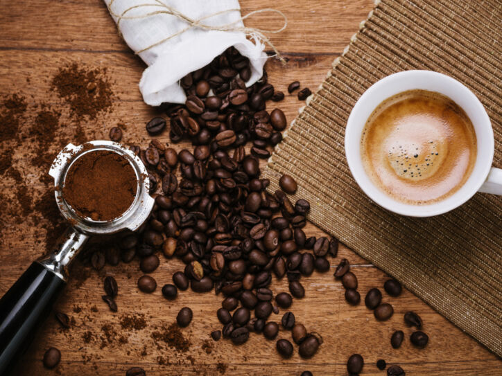 Kaffeebohnen, Espresso mit Crema und Espressopulver liegen auf einem Brett