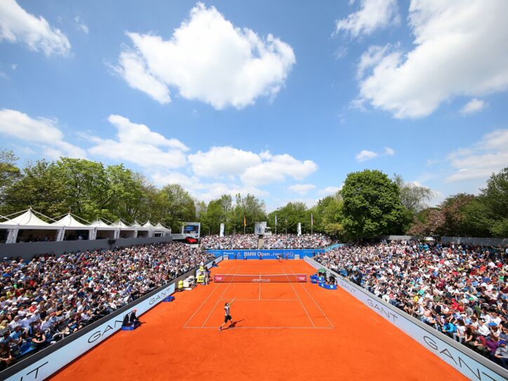 Tennisspieler spielen auf einem Sandplatz, umgeben von zahlreichen Zuschauern.