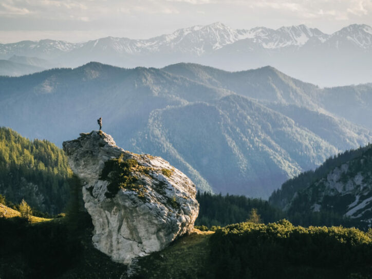 Eine Person beim Wandern auf einem Felsen umgeben von Bergen