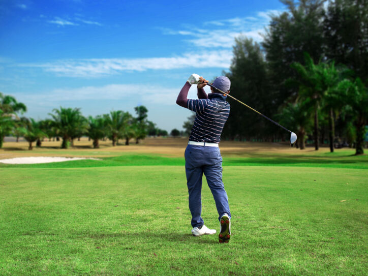 Ein Golfspieler von hinten auf einem Golfplatz, im Hintergrund Palmen