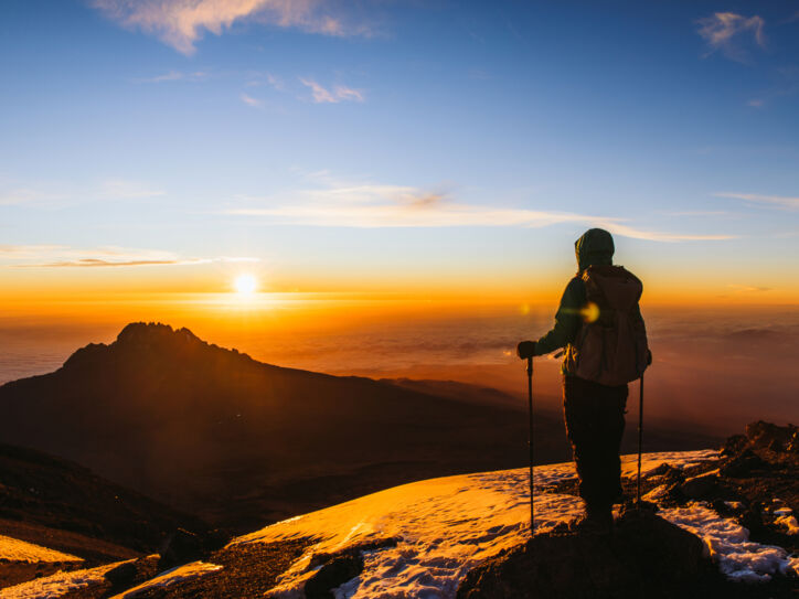 Eine Wanderin blickt vom Gipfel des Kilimandscharo in den Sonnenaufgang