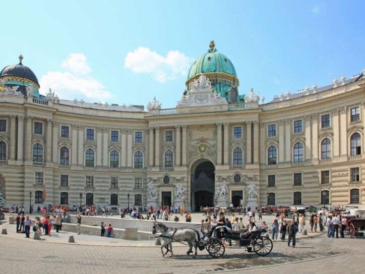 Personen und Pferdekutschen auf einem Platz vor der Wiener Hofburg