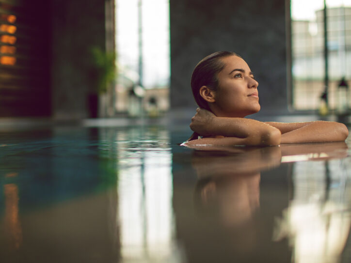 Eine junge Frau entspannt am Beckenrand eines Pools in einem Wellnessbereich.