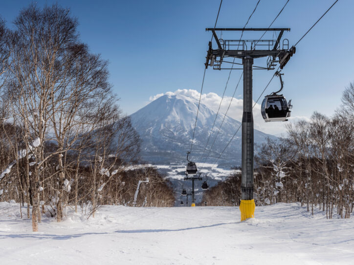 Skilift und Schneelandschaft mit Bäumen. Im Hintergrund ein schneebedeckter Berg und blauer Himmel.