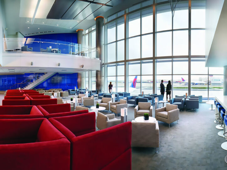 Geräumige Flughafen-Lounge in den Farben Rot, Weiß und Blau mit Blick aufs Rollfeld durch Panoramafenster.