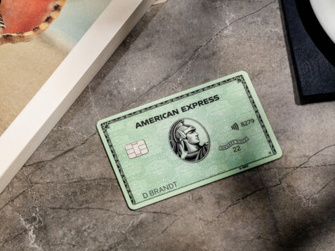 ine grüne American Express Kreditkarte liegt auf einem grauen Marmortisch neben einem Buch.