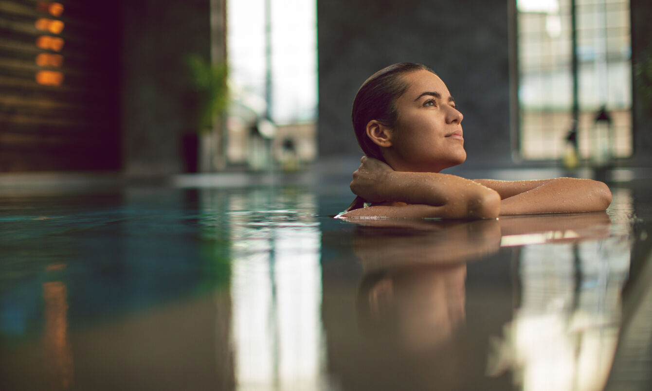 Eine junge Frau entspannt am Beckenrand eines Pools in einem Wellnessbereich.