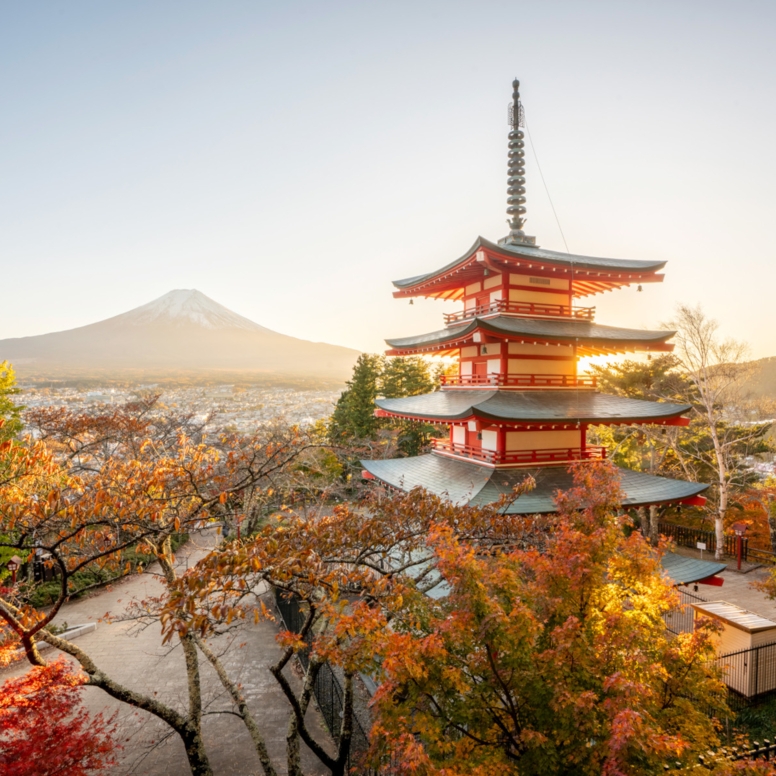 Ein mehrstöckiger, japanischer Tempel mit roten Ornamenten, im Hintergrund eine Stadt am Fuße des Mount Fuji