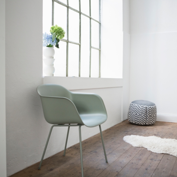 Ein grüner Stuhl aus Plastik steht an einer Wand neben einem Fenster