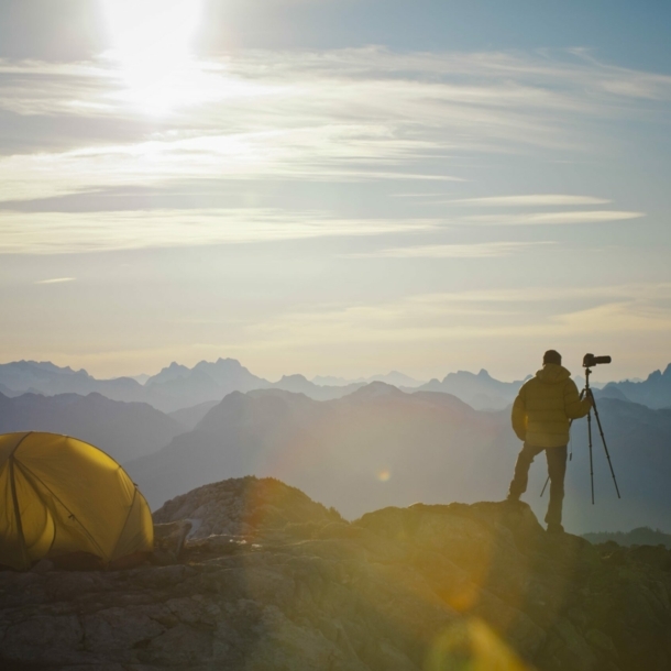 Ein Zelt und ein Mann mit Fotoapparat vor einer Hochgebirgskulisse