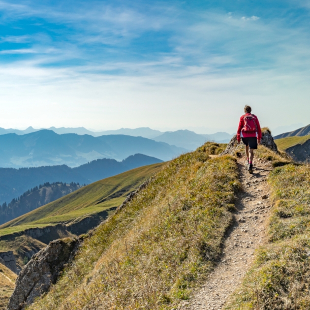 Rückansicht einer Person mit rotem Rucksack auf einem Wanderweg in den Bergen