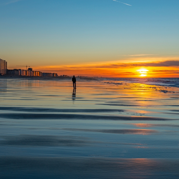 Eine Person am Strand bei Sonnenuntergang vor einer Stadt im Hintergrund