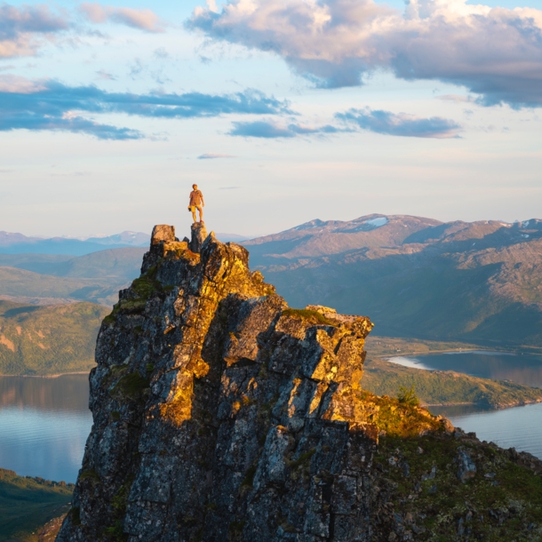 Eine Wanderin auf einem Felsen an einem Fjord.