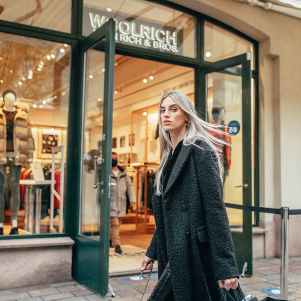 Eine Frau in langem schwarzen Mantel läuft an einem winterlichen Schaufenster vorbei