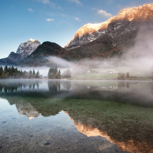 Ein See mit glasklarem Wasser über dem Nebelschwaden liegen vor Bergpanorama in der Dämmerung