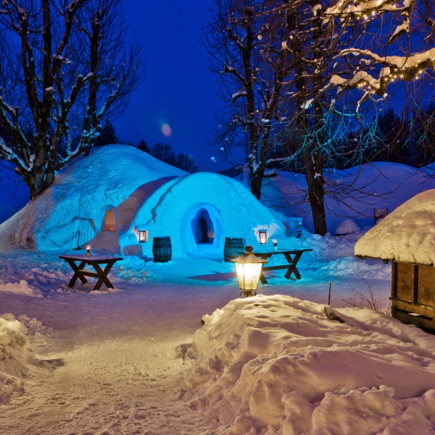 Ein Iglu in einer schneebedeckten Umgebung, daneben Tische und Bäume