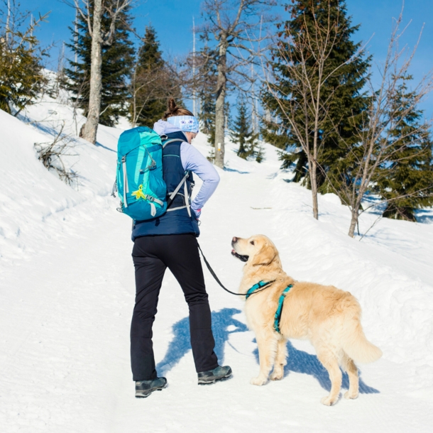 Frau mit Wanderrucksack und Hund im Schnee