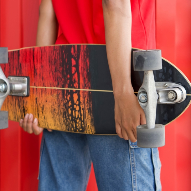 Rückansicht einer Frau, die ein Longboard hinter dem Rücken hält