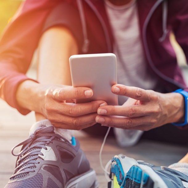 Sportlich gekleidete Person sitzt auf dem Boden und hält ein Handy in der Hand.