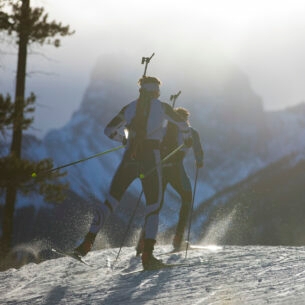 Drei Männer auf Skiern mit einem Biathlon-Gewehr auf dem Rücken fahren durch den Schnee.