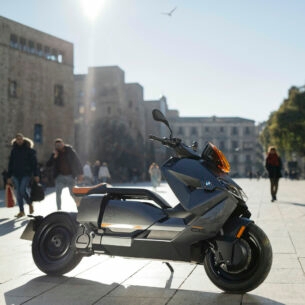 Ein grauer BMW CE 04 parkt vor Palmen in einem Fußgängerbereich.