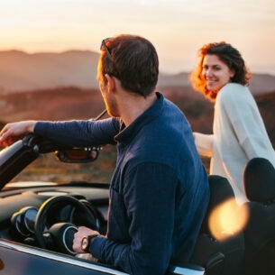 Rückansicht eines Paares auf Reise, das aus einem Cabriolet in eine Wüstenlandschaft bei Sonnenuntergang schaut