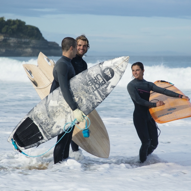 Drei Menschen stehen in Neoprenkleidung und Surfbrettern im Wasser.