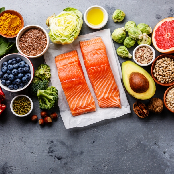 Gesunde Lebensmittel wie Lachs, Avocado, Granatapfel und mehr nebeneinander.