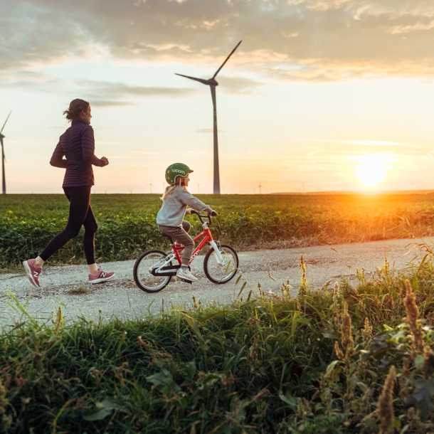 Eine joggende Frau ist mit einem kleinen Mädchen auf dem Fahrrad bei Sonnenuntergang unterwegs