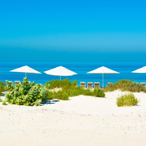 Sandstrand und blaues Meer mit Sonnenliegen und Sonnenschirmen