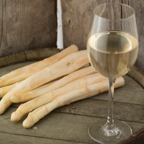 Ein Glas Wein und mehrere Stangen Spargel auf einem Fass Wein