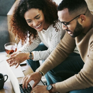 Eine Frau und ein Mann sitzen an einem Couchtisch mit Abrechnungen vor einem Laptop