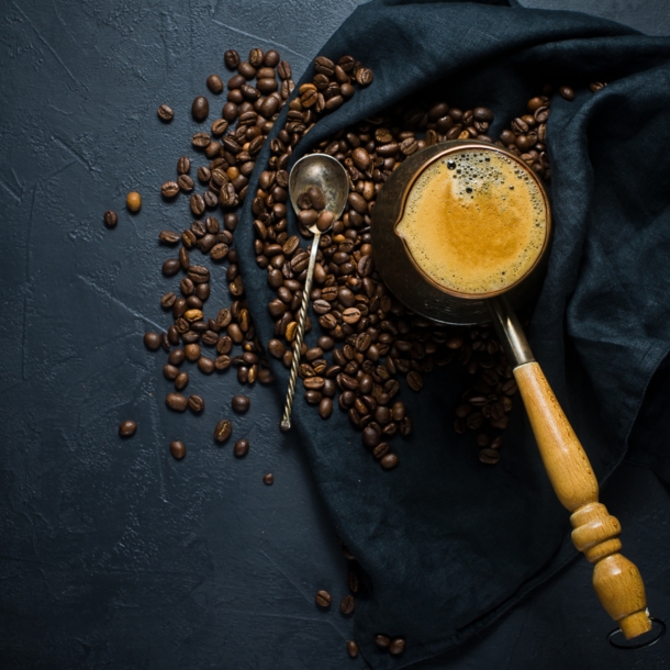 Geröstete Bohnen und frisch gebrühter Kaffee auf einem dunklen Tuch angerichtet