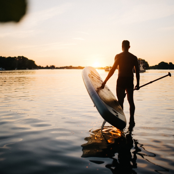 Mann trägt ein SUP Board ins Wasser