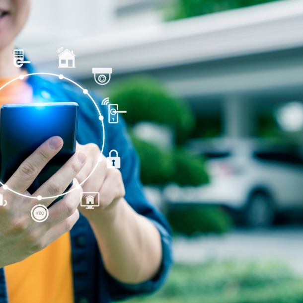 Person mit Smartphone, im Hintergrund ein Auto vor einer Garage