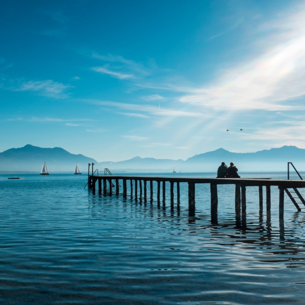 Zwei Personen sitzen auf einem Holzsteg auf dem Chiemsee