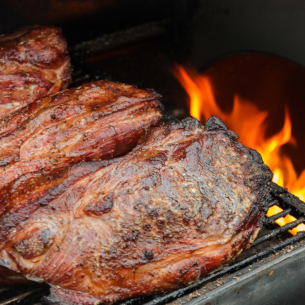 Fleisch wird indirekt neben einer Flamme im Grill gegrillt