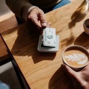 Kontaktlose Zahlung eines Cappuccinos mit einer silbernen Kreditkarte