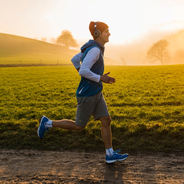 Ein junger Mann joggt im Morgengrauen an einer Wiese entlang