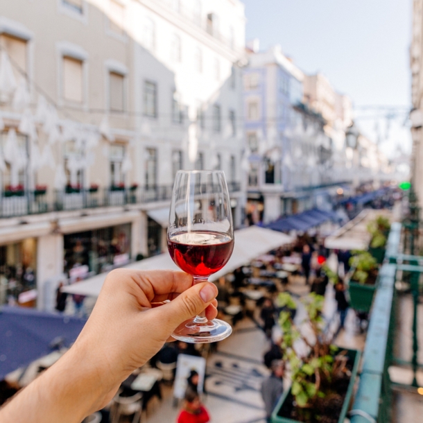 Eine Hand hält ein Glas Portwein oberhalb einer belebten Gasse in die Luft