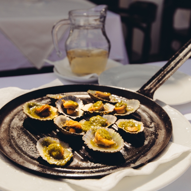 Napfschnecken mit grüner Soße, angerichtet auf einer Grillpfanne auf einem Restauranttisch