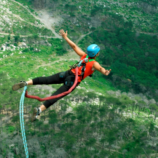 Eine Frau springt von einer Klippe am Bungeeseil in den Abgrund.