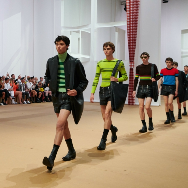 Männliche Models in Ledershorts laufen in Reihe auf einem Catwalk