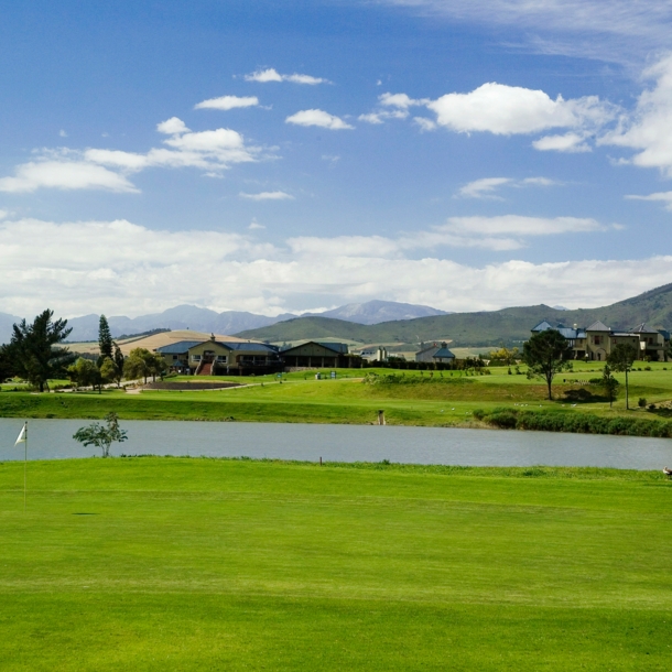 Blick auf einen Golfplatz mit See und Bergen im Hintergrund