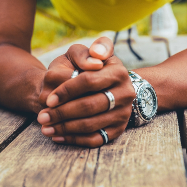 Gefaltete Männerhände mit silbernen Ringen und einer Uhr am Handgelenk