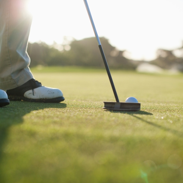 Nahaufnahme von einem Golfschläger, dahinter ein weißer Golfball auf einem grünen Rasen