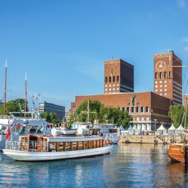 Blick auf das rote Rathaus von Oslo mit Backsteintürmen vom Wasser aus, im Vordergrund Segelboote