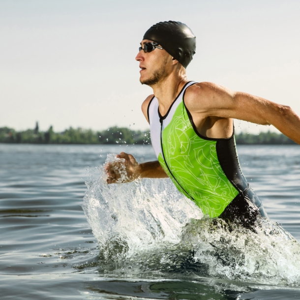 Ein durchtrainierter Triathlet mit Badekappe und Schwimmbrille rennt ins Wasser